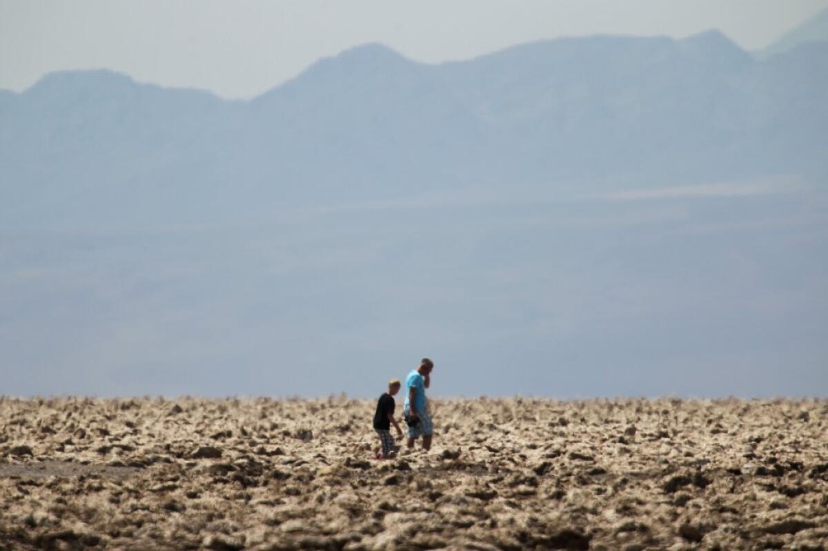 Tourists walk in an area known as The Devil's Golfcourse in Death Valley. Scientists have found that a cyanobacterium that helps stabilize desert soil is imperiled by climate change.