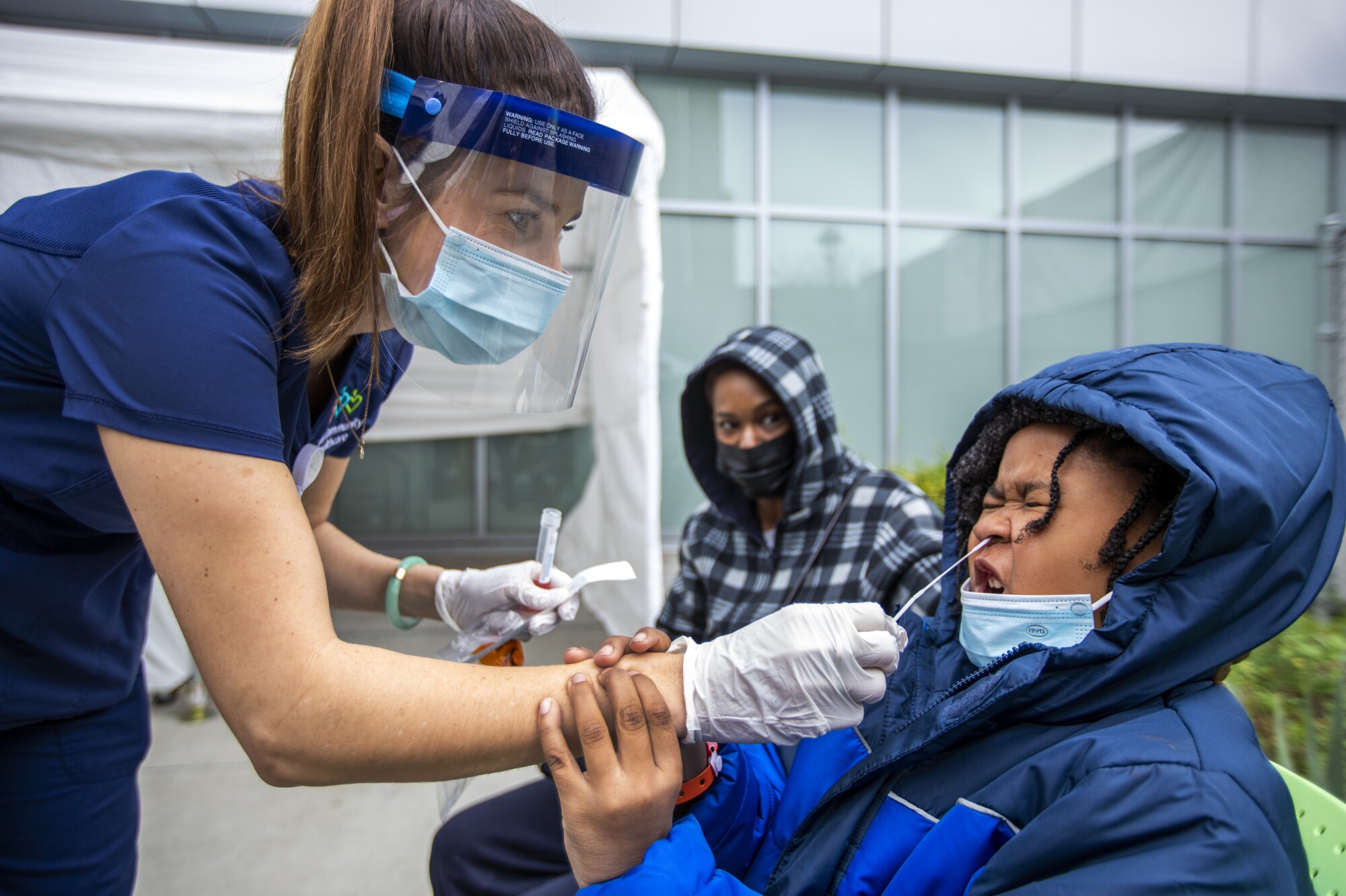 A nurse uses a nasal test swab on a boy as his mother watches
