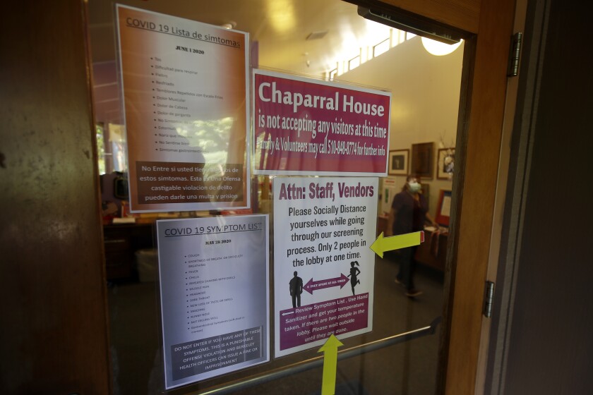 Signs with info on COVID-19 symptoms, social distancing rules and no-visitation policies posted on a nursing facility's door