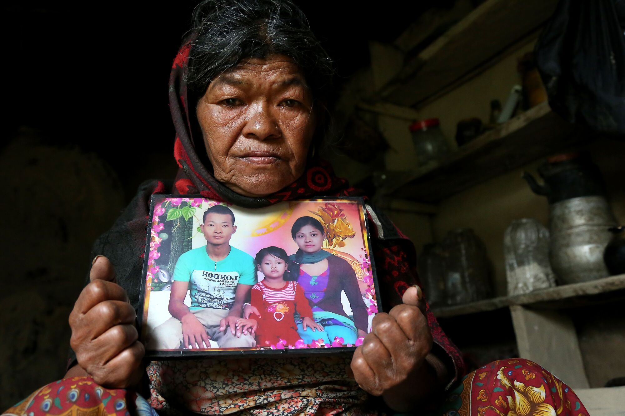 Subitra Bhandari, crouching in her one-room home where she lives alone, holds a photo of her son Tejendra and family.