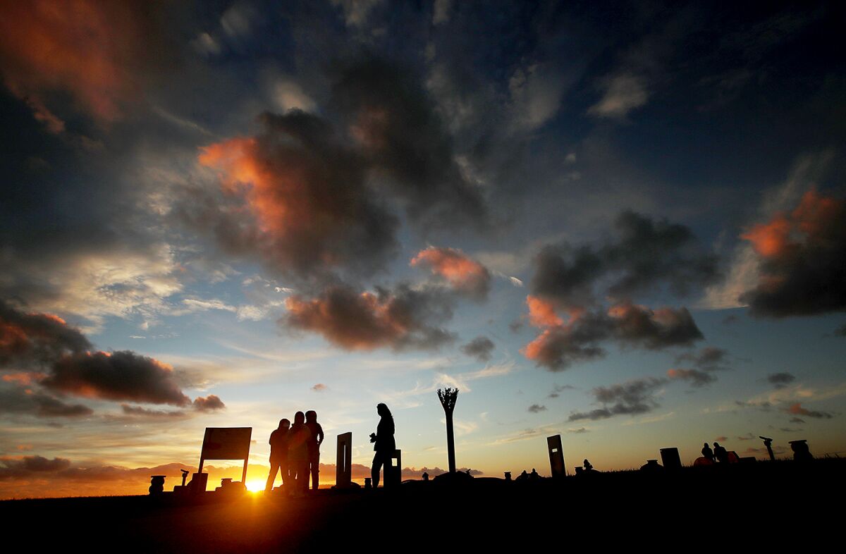 People are silhouetted by a sunset as patchy clouds give way to clear sky. 