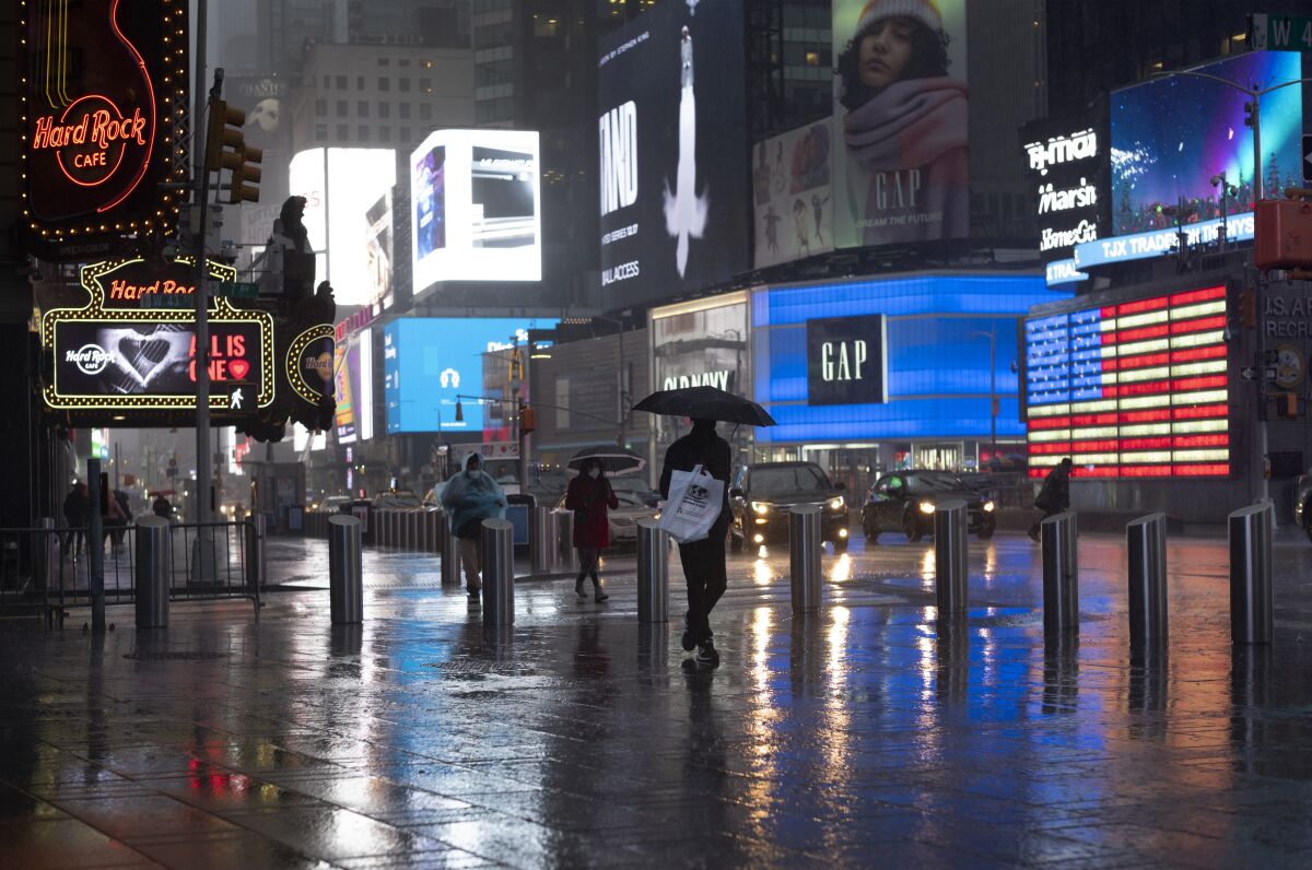 FILE - In this Nov. 30, 2020, file photo, shoppers walk in a rainstorm through New York's Times Square. The job market is slowing down as the fall surge in the virus puts severe strain on the economy and health care system. (AP Photo/Mark Lennihan)