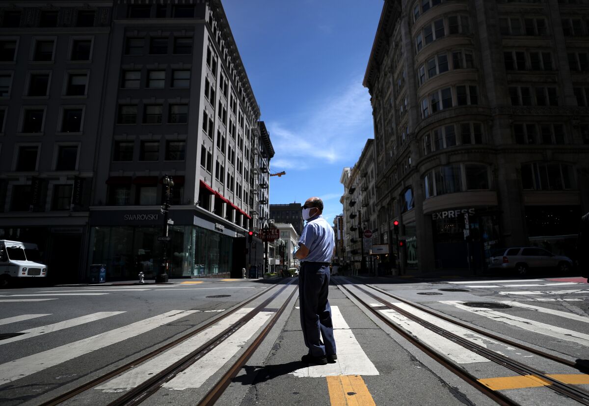 A U.S. Postal Service letter carrier stands in the middle of Powell Street in San Francisco. San Francisco, San Mateo and Marin plan to incrementally ease their social-distancing restrictions starting Monday.