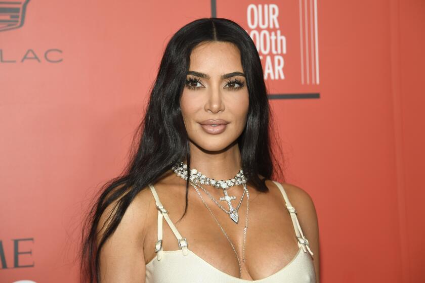 Kim Kardashian poses in a white dress and chunky cross necklace.