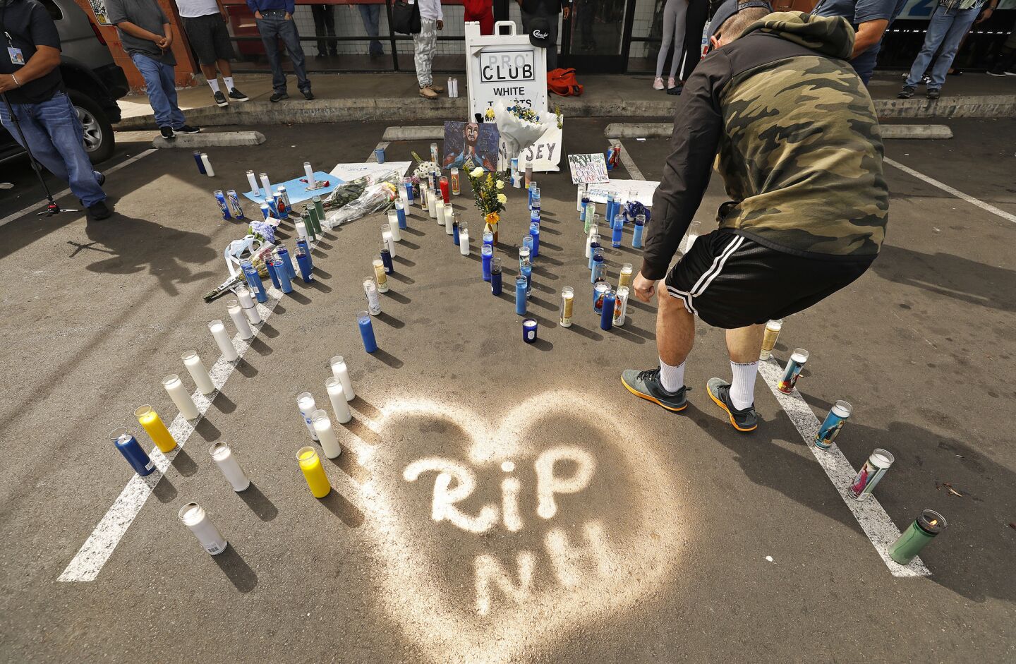 Jesse Junco, 28, from San Bernardino lights candles Monday morning at one of a few growing memorials in front of the Marathon Clothing store.