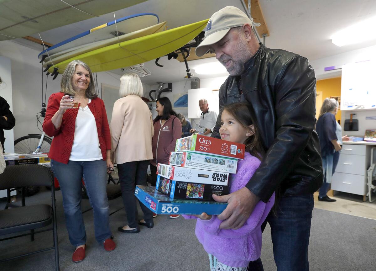 Puzzler Jazzlyn Lewis, with dad John, takes home a stack of puzzles Friday from the garage of Mary Fewel's Costa Mesa home.