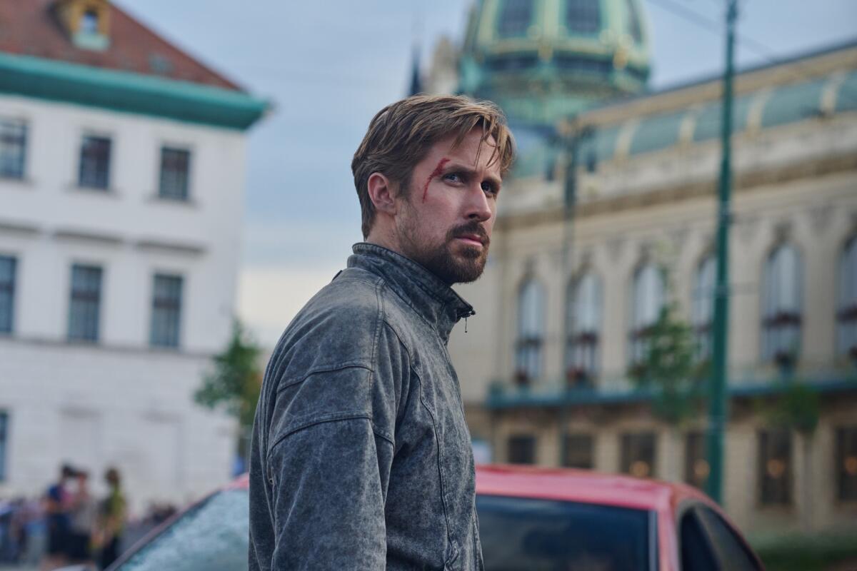 A bearded man with a cut on his forehead stands in a street.