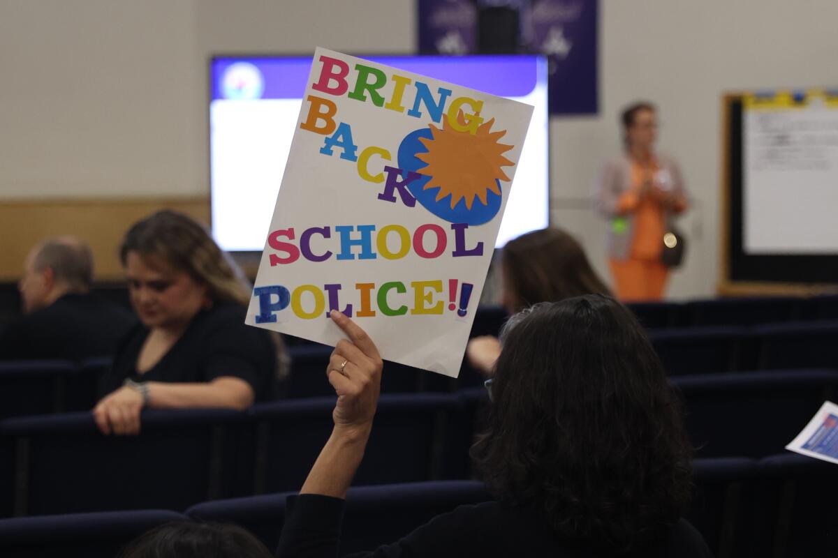 An L.A. Unified student's parent holds a "Bring Back School Police" sign. 