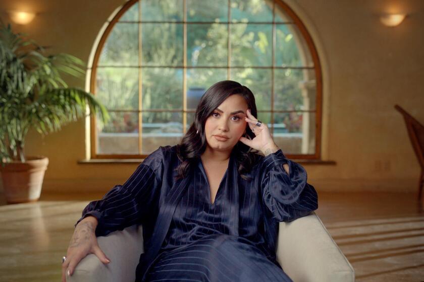 Demi Lovato wearing a silk outfit, sitting in a white armchair 