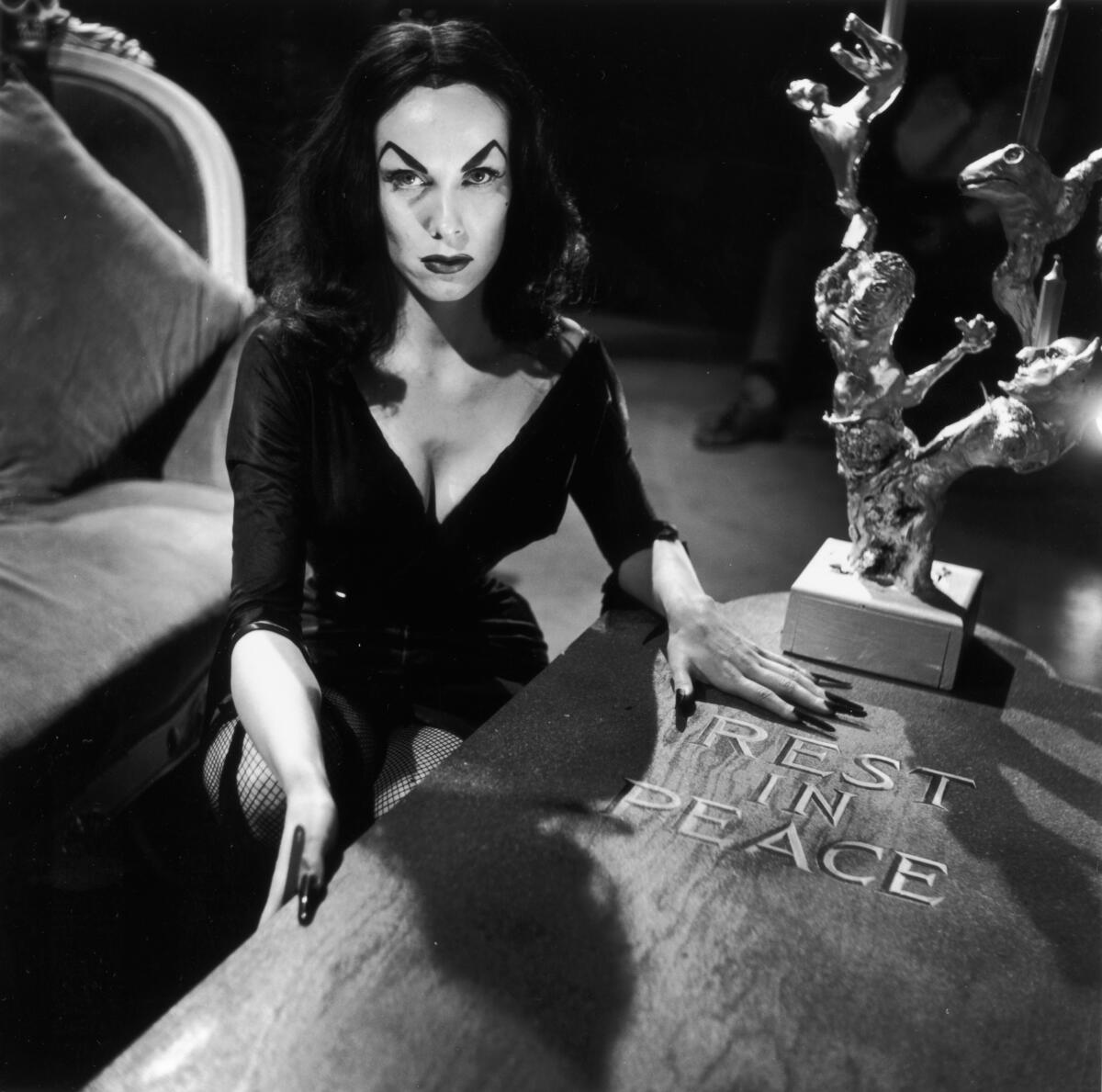 A publicity photo of actress and TV host Vampira, real name Maila Nurmi, crouching beside a wooden coffin, circa 1956.
