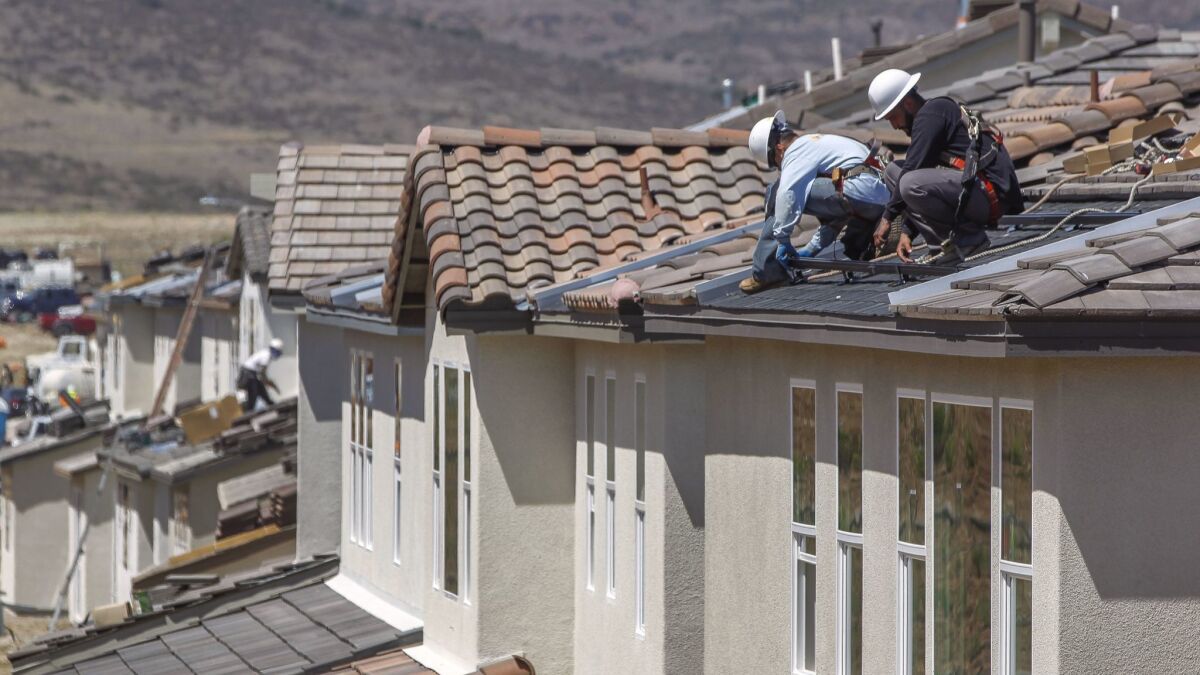 Workers install a solar racking system on the rooftop of a new home in the Weston housing development in Santee in May 2018.