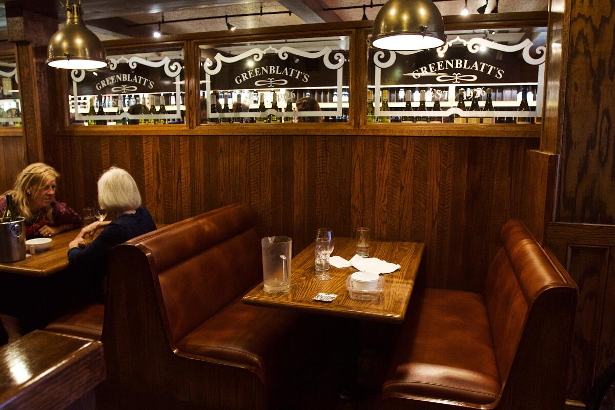 Two people talk over a table in a booth in a restaurant.