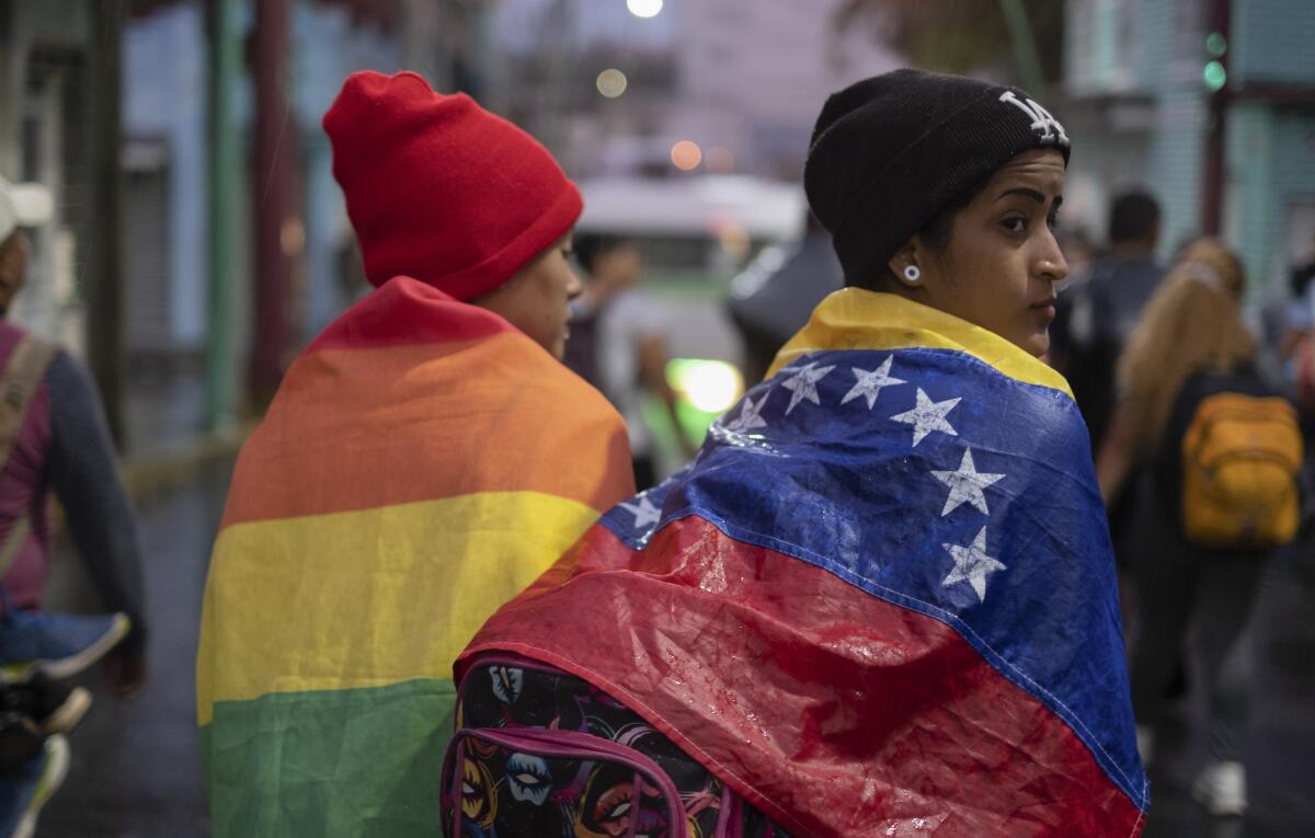 ARCHIVO - Una persona envuelta en una bandera venezolana camina con un grupo de migrantes 