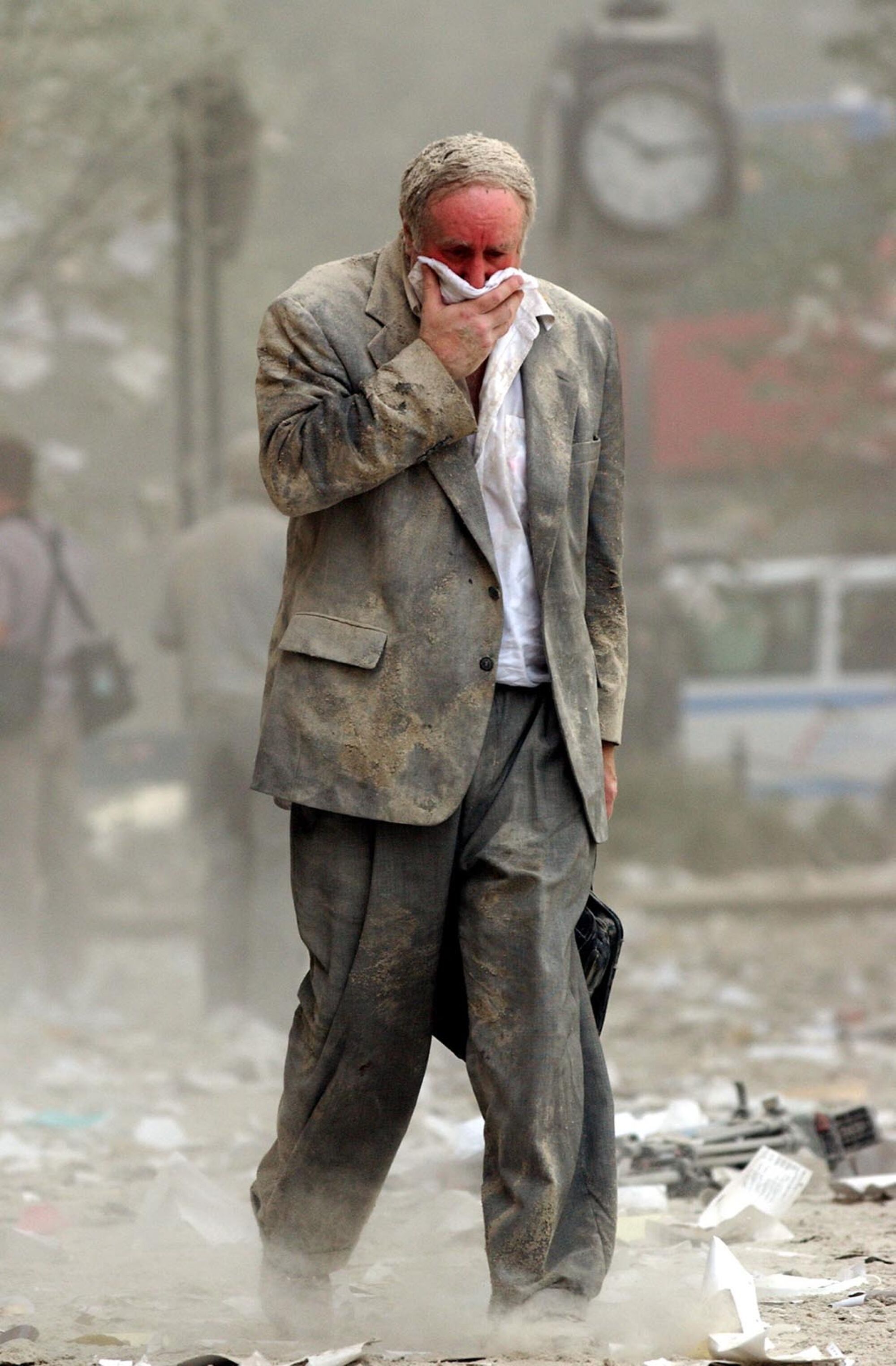 A man covers his mouth as he walks amid dust and debris