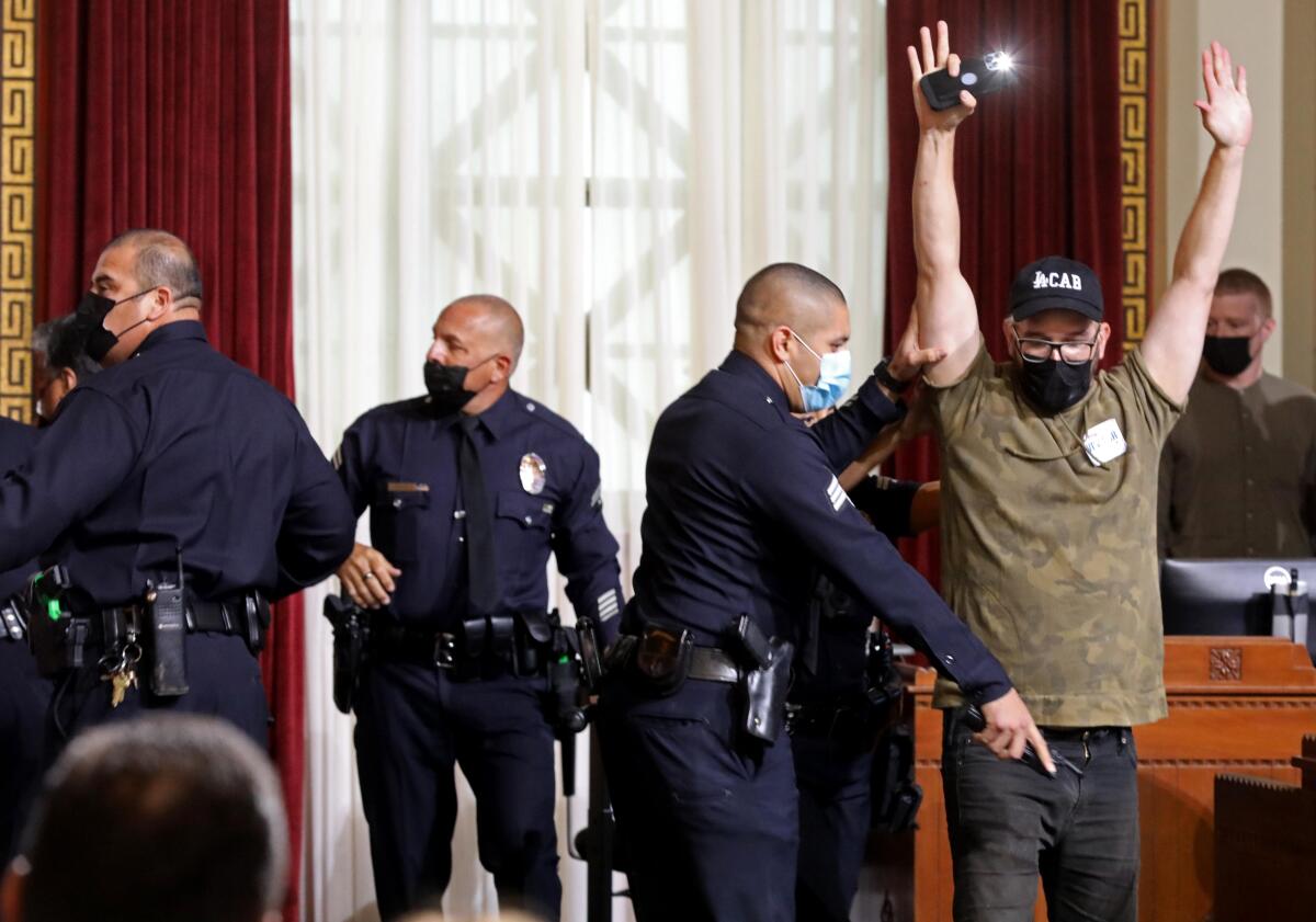 Ricci Sergienko raises his arm while a police officer holds one of Sergienko's arms and points.