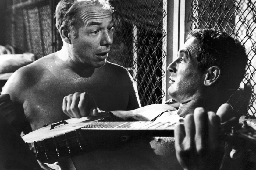 Paul Newman, playing a banjo, and George Kennedy in the film "Cool Hand Luke" directed by Stuart Rosenberg. Newman won a best actor Oscar, and Kennedy won a best supporting actor Oscar for their roles in the film.