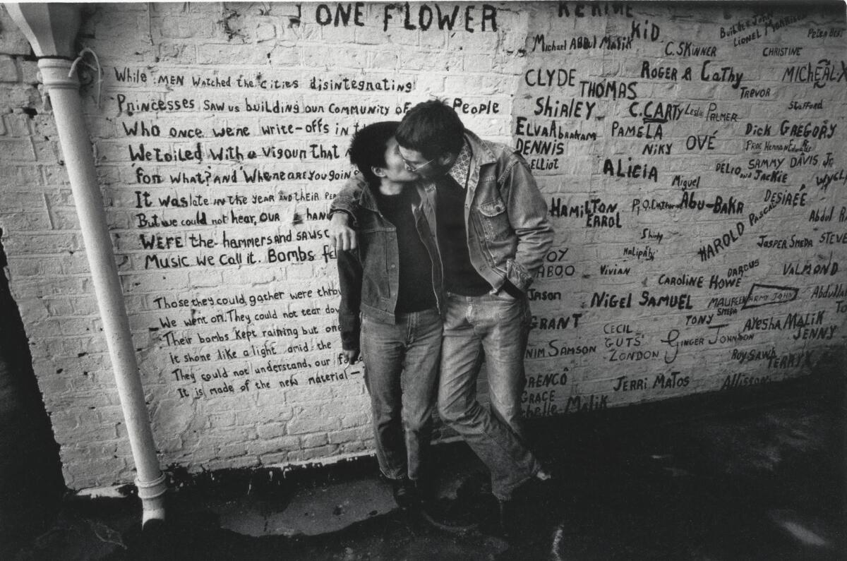  John and Yoko kiss in front of a white wall with writing on it.