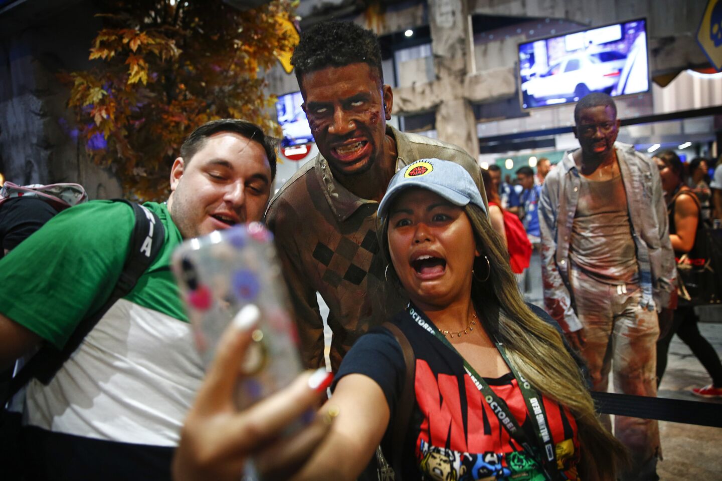 At left, Tim Walker, 26, of San Diego, and Julia Homitano, 27, of San Diego, take a selfie with zombies while waiting in line at "The Walking Dead" booth.