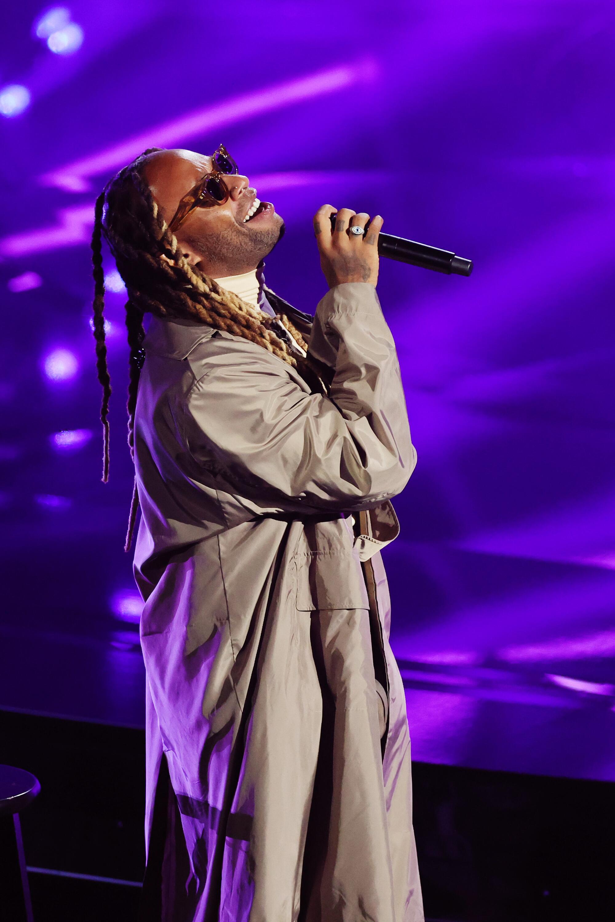 Ty Dolla Sign, in sunglasses and a long tan duster, sings into the microphone.
