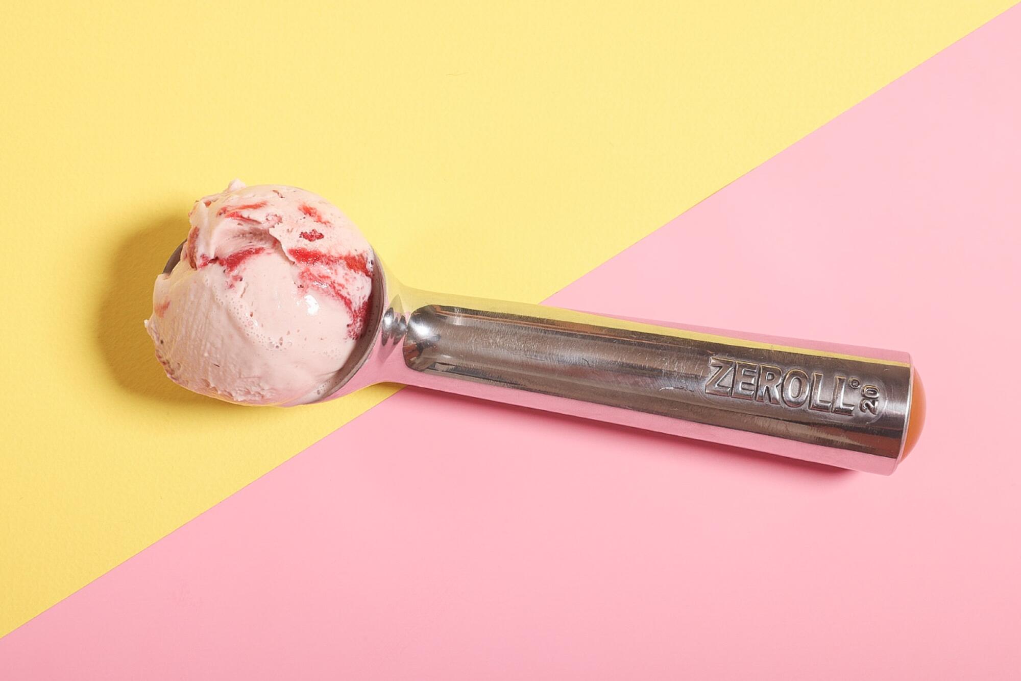 The Zeroll ice cream scoop holds a helping of the frozen treat on a yellow and pink background