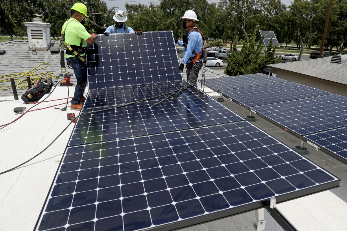 Men in hard hats and tool belts stand on a roof with solar panels.