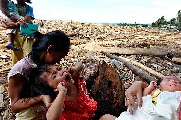 A family sit on logs washed ashore in a village devastated by rampaging flooding near Iligan City.