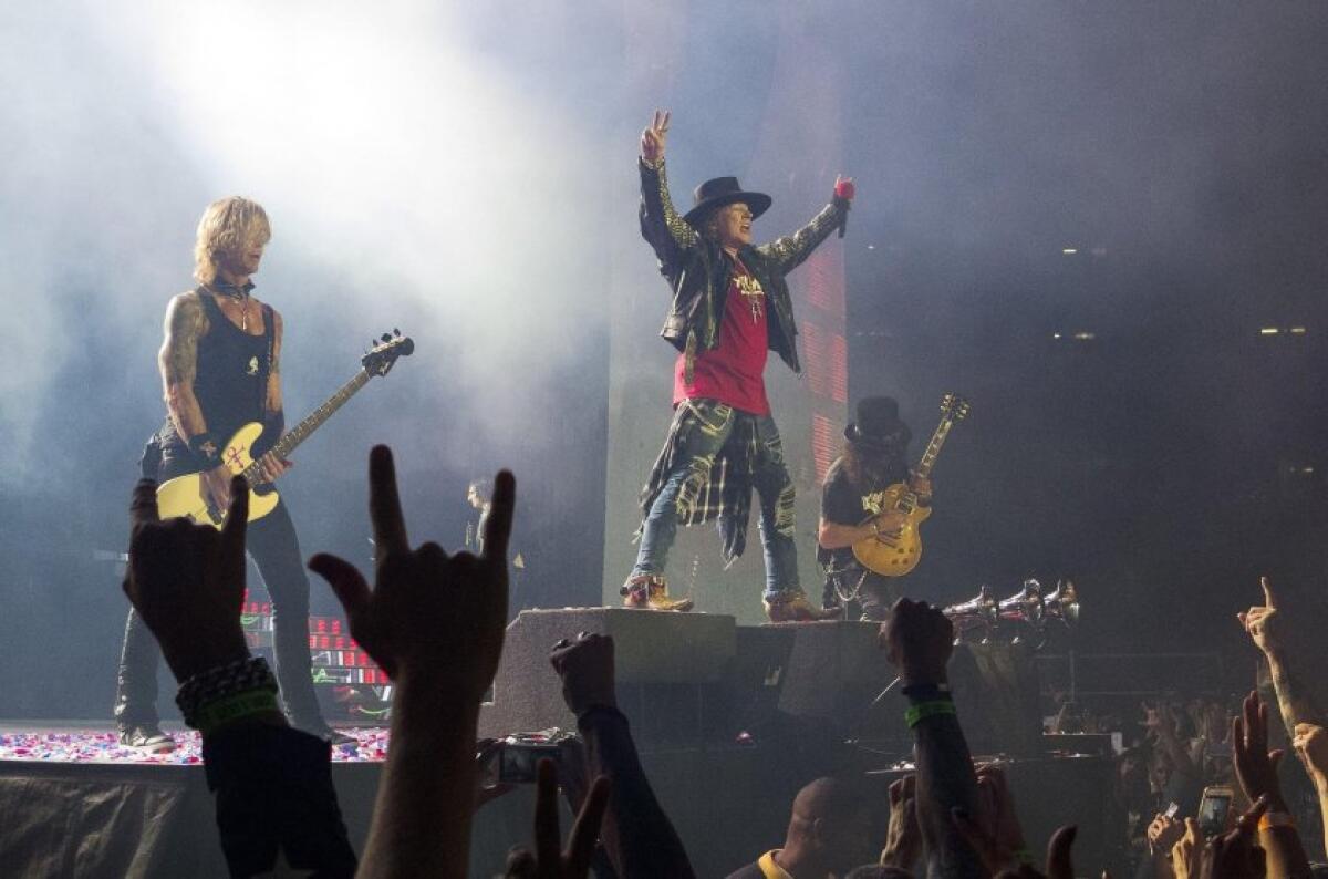 Duff McKagan, left, Axl Rose and Slash stand on platforms of varying height