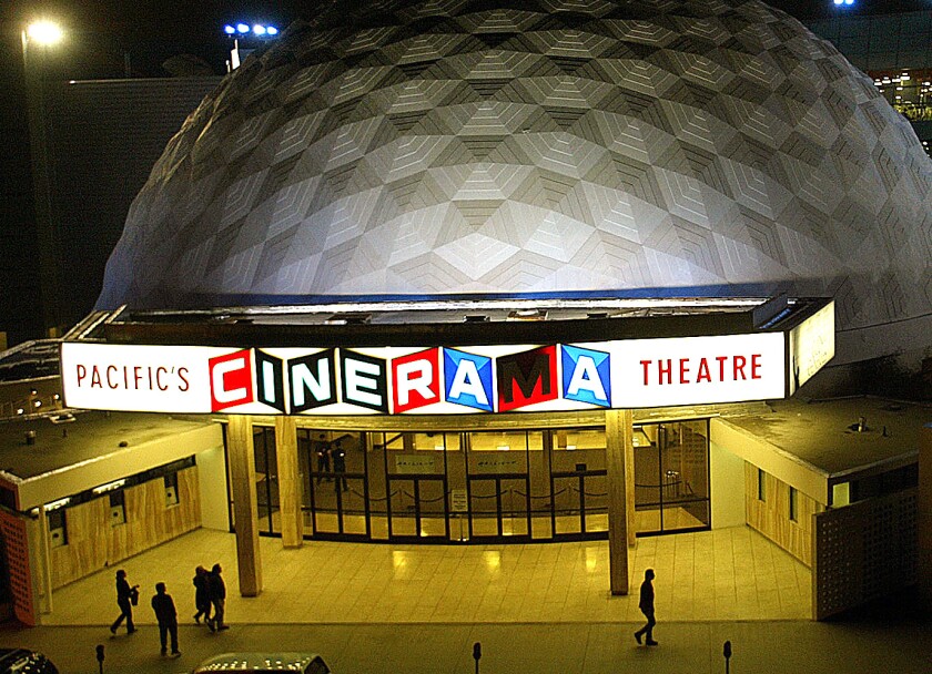 People walk past a movie theater with a large white dome.