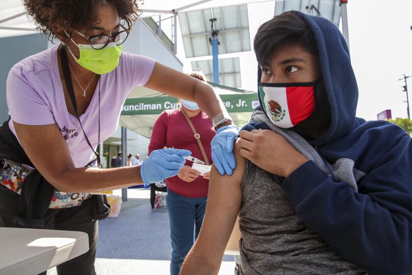 Los Angeles, CA - June 24: Nurse Marie Eddins, left, administers COVID19 vaccine to 14-year-old Emanuel Coyote at mobile clinic held at Los Angeles City Councilman Curren Price's district office. After getting vaccine Coyote got a free pair of ``Beats by Dre'' headphones at Councilman Curren Price's district office on Thursday, June 24, 2021 in Los Angeles, CA. (Irfan Khan / Los Angeles Times)