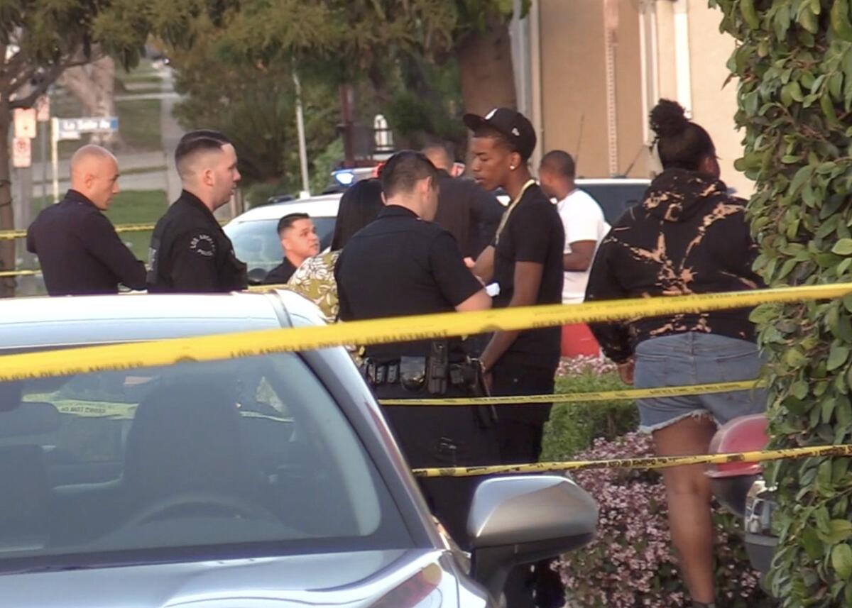 Police and residents stand behind yellow police tape in a residential neighborhood.