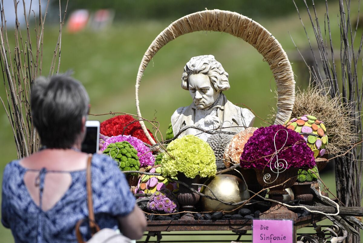 A woman looks at a sculpture of Beethoven surrounded by flowers.
