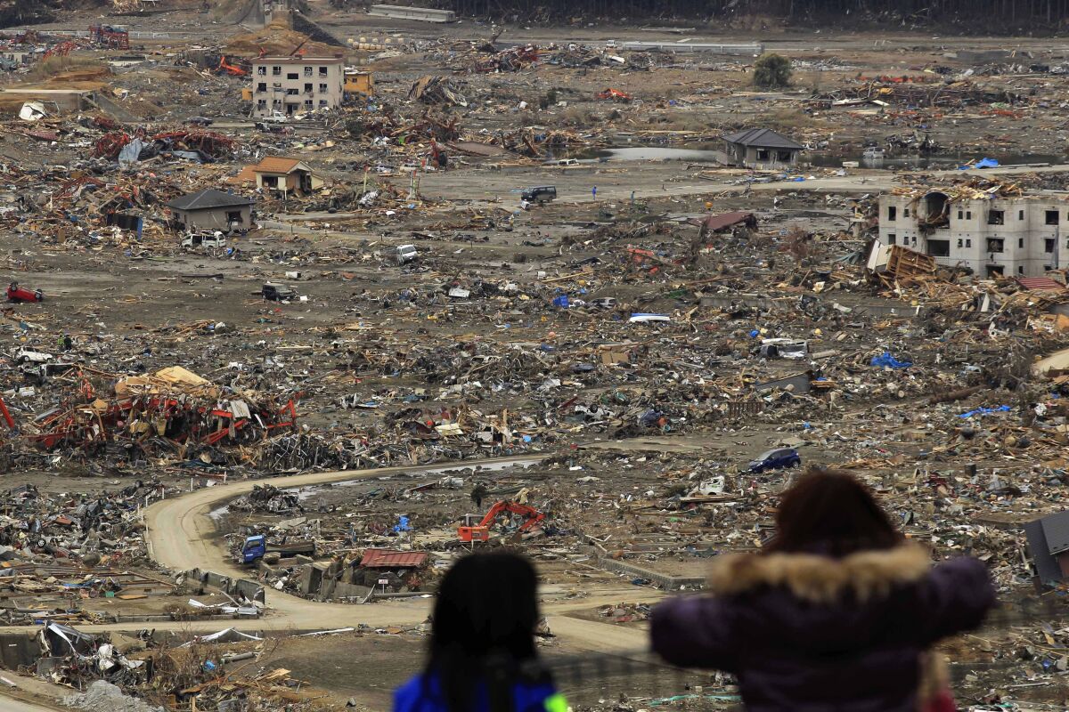 Two people look at a debris-filled landscape after a 2011 tsunami in northern Japan