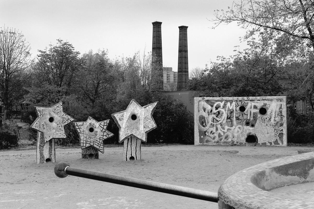 A stark, empty playground in Berlin with smokestacks behind.