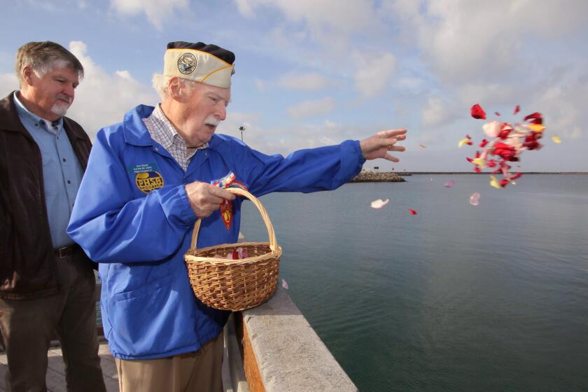 Pearl Harbor survivor Joe Walsh, 97, of Fallbrook, tosses flower petals in the water during the Pearl Harbor memorial event at the Oceanside Harbor's fishing pier. At left is his son Tom Walsh, of Oregon.