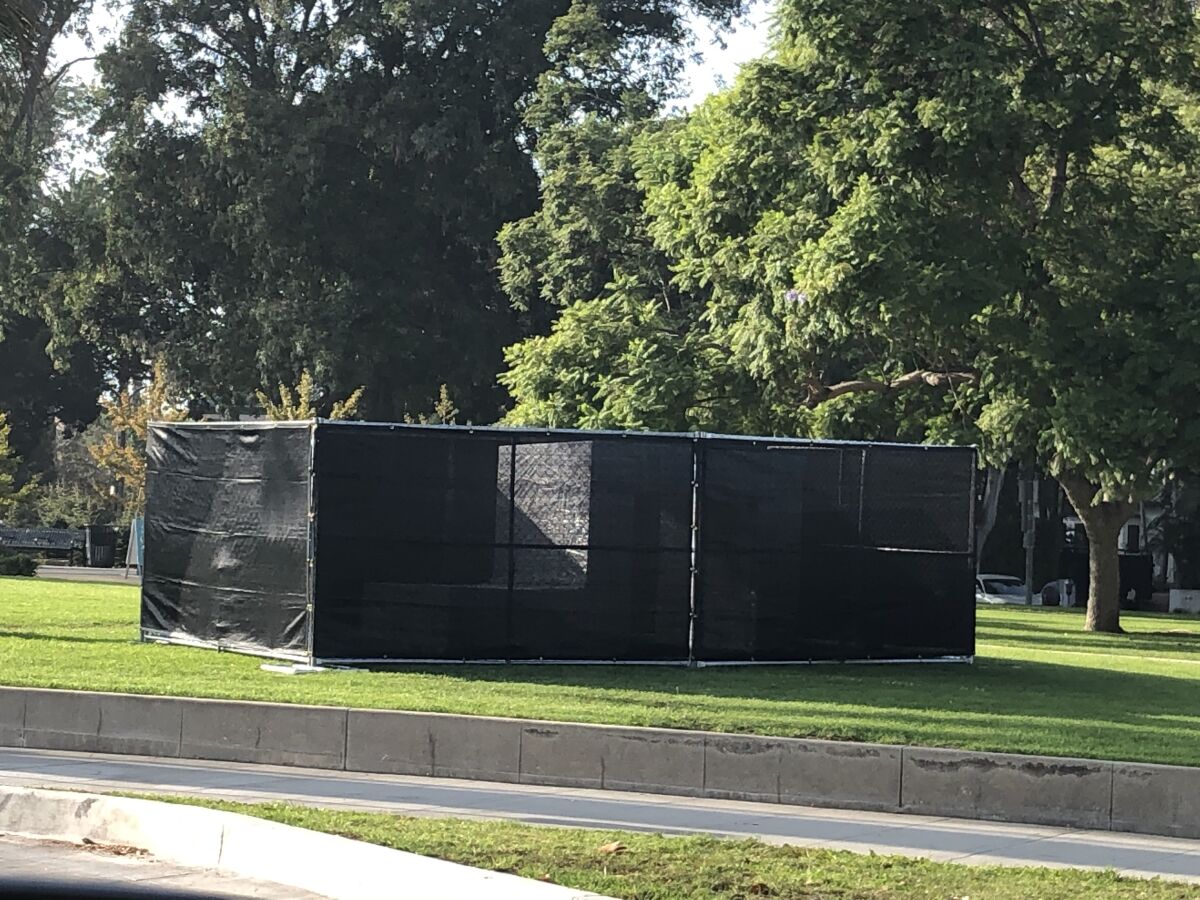 A black construction fence in the middle of a grassy park