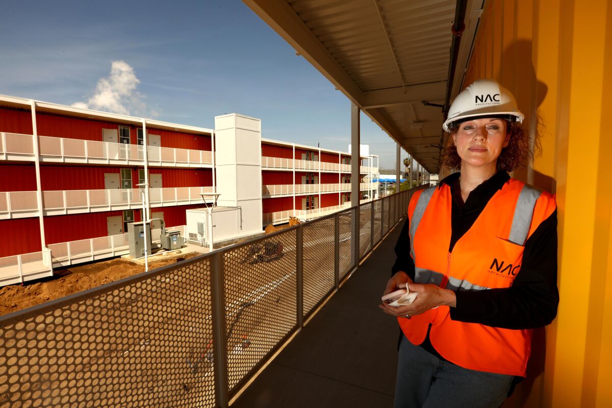 Architect Louise Griffin, in hard hat and safety vest, stands on the outdoor terrace of a shipping container tower
