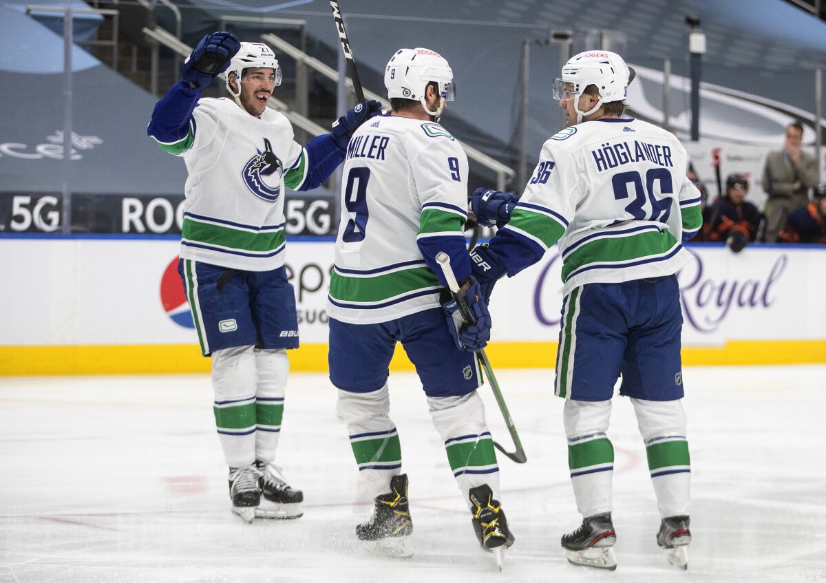 Vancouver Canucks' Travis Hamonic (27), J.T. Miller (9) and Nils Hoglander (36) celebrate a goal against the Edmonton Oilers during the first period of an NHL hockey game Thursday, May, 6, 2021, in Edmonton, Alberta. (Jason Franson/The Canadian Press via AP)