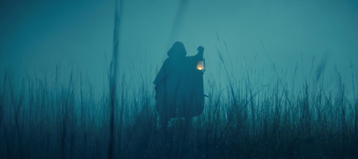 A cloaked figure in the fog holding a light