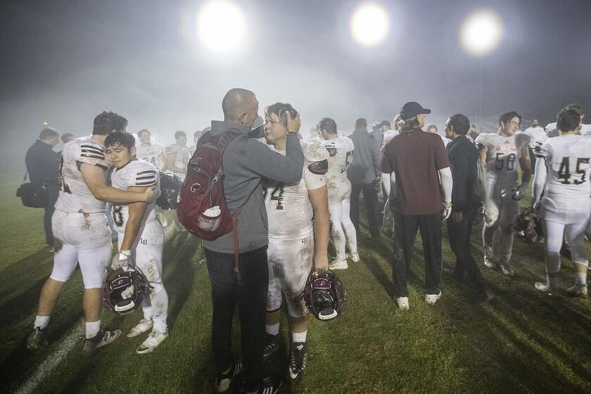 Assistant coach Darren Crawford hugs Hunter Davis following Laguna Beach High's 48-6 loss at Lakewood Artesia in a CIF Southern Section Division 12 semifinal game on Friday.