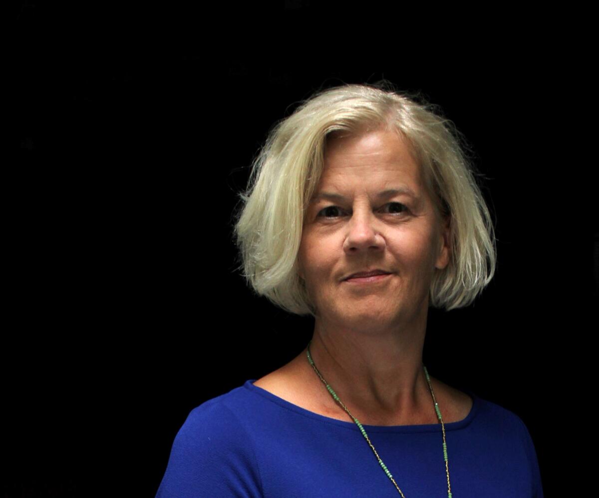 A woman with silver hair, a bright blue top and a necklace.