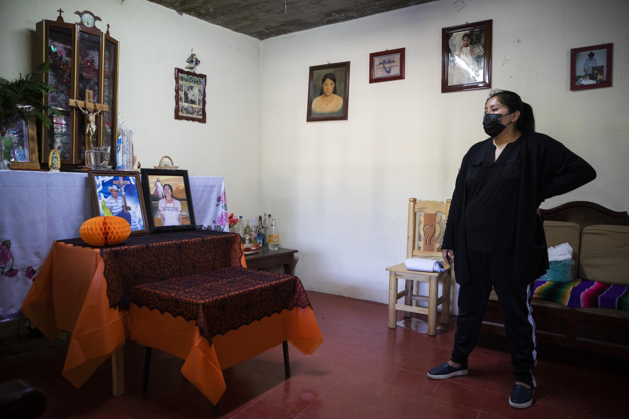 A woman dressed in black speaks next to an altar with photos