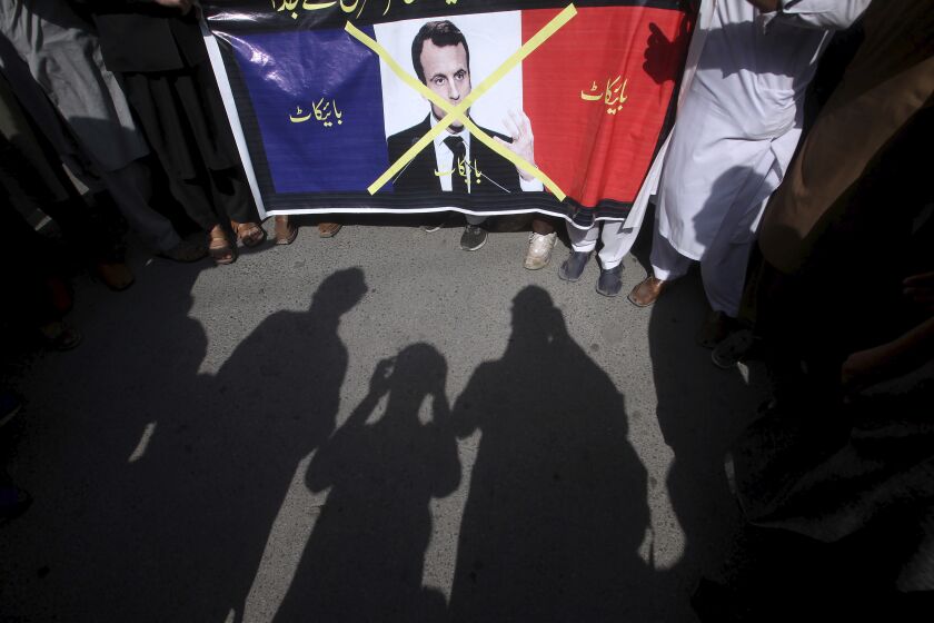 Supporters of the religious student group, Islami Jamiat Tulba, hold a representation of the French flag with a defaced image of French President Emmanuel Macron and Urdu writing which reads, "Down with France," during a protest against the publishing of caricatures of the Prophet Muhammad they deem blasphemous, in Peshawar, Pakistan, Tuesday, Oct. 27, 2020. (AP Photo/Muhammad Sajjad)