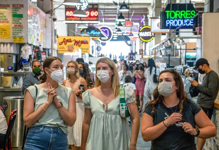 People walking an aisle at Grand Central Market are mostly masked.