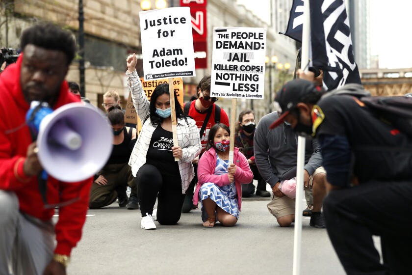Abigail Garcia, 7, right, takes a knee with her mother Judith Garcia and other protestors during a peaceful protest on Tuesday, April 13, 2021 in downtown Chicago, demanding justice for Daunte Wright and Adam Toledo, who were shot dead by police. (AP Photo/Shafkat Anowar)