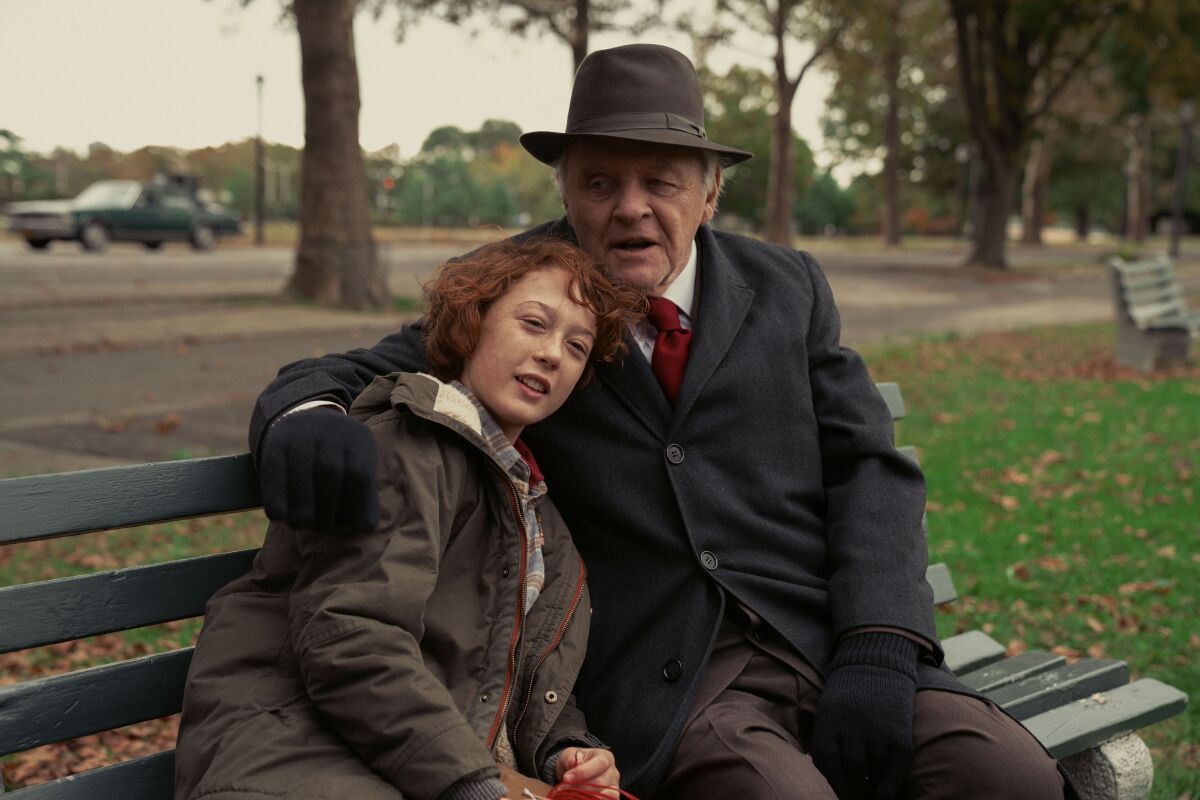 A boy sits on a park bench with his grandfather's arm around him in a scene from 