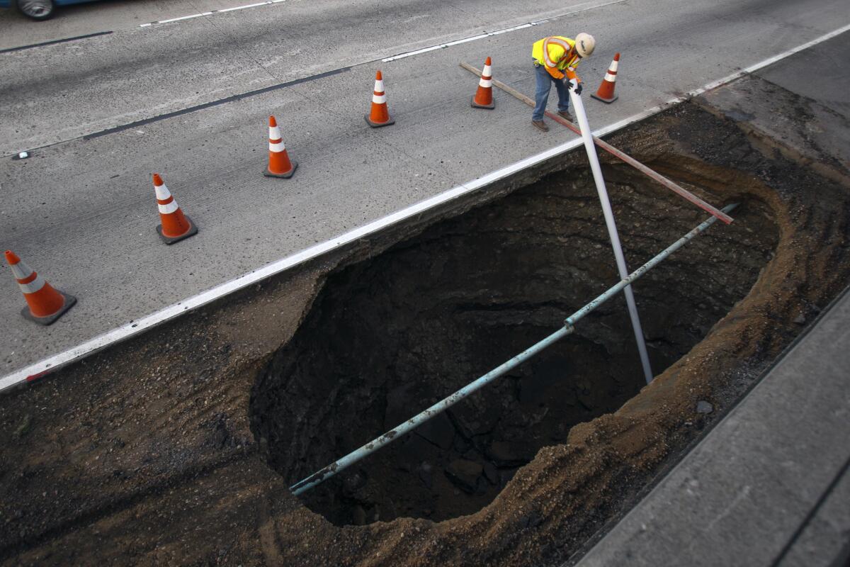 A worker places a pipe into a large sinkhole as he and other crews fix the hole next to the eastbound lanes of Interstate 8 in San Diego.