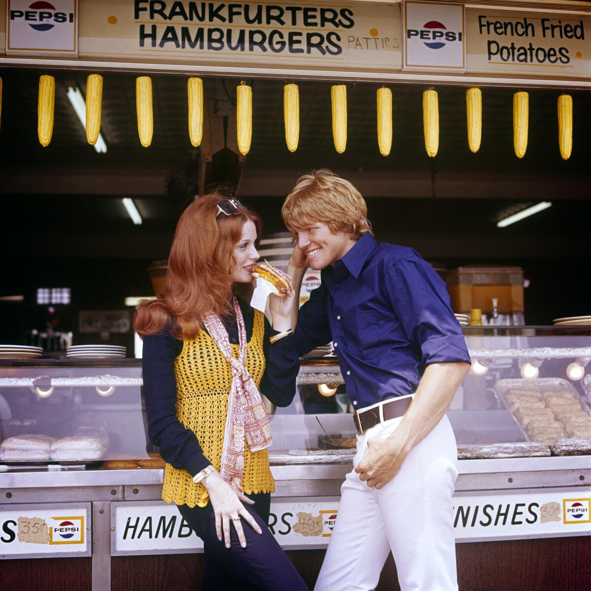 1970s Redhead Woman Wearing Crochet Vest Eating A Hot Dog With Blonde Man At Concession Hamburger Stand On Coney Island Ny USA (Photo by Photo Media/Classicstock/Getty Images)