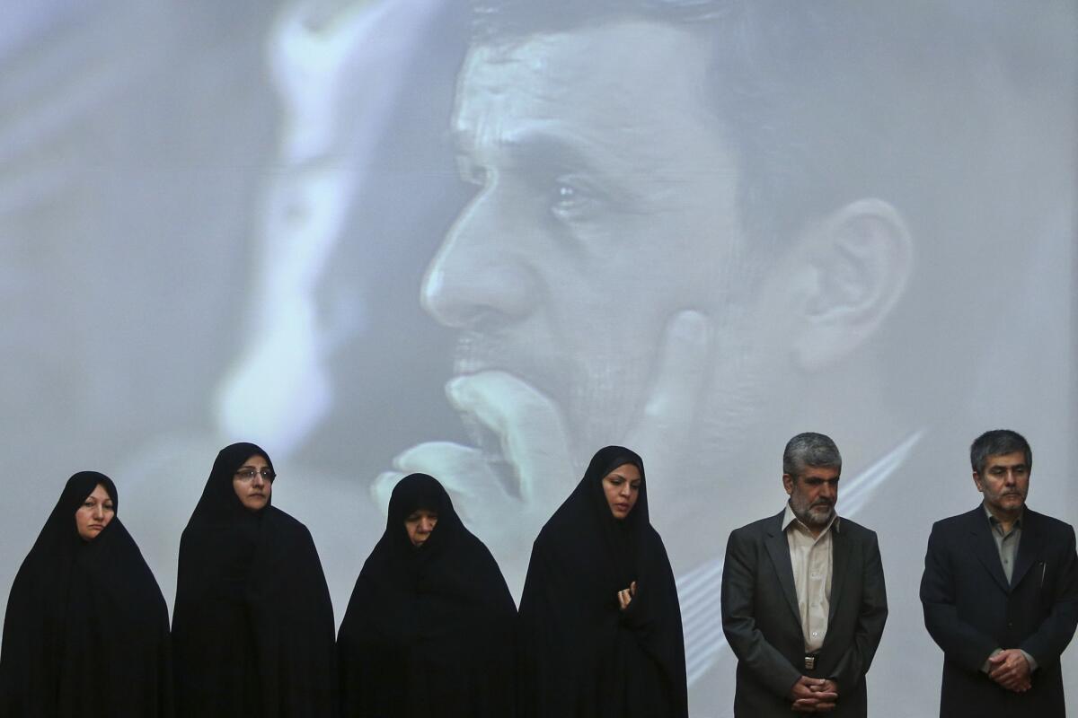 Family members of Iran's slain nuclear scientists and workers stand with the head of Iran's Atomic Energy Organization, Fereydoun Abbasi, right, Tuesday in a ceremony marking Iran's National Day of Nuclear Technology. President Mahmoud Ahmadinejad is seen on a giant screen behind them.