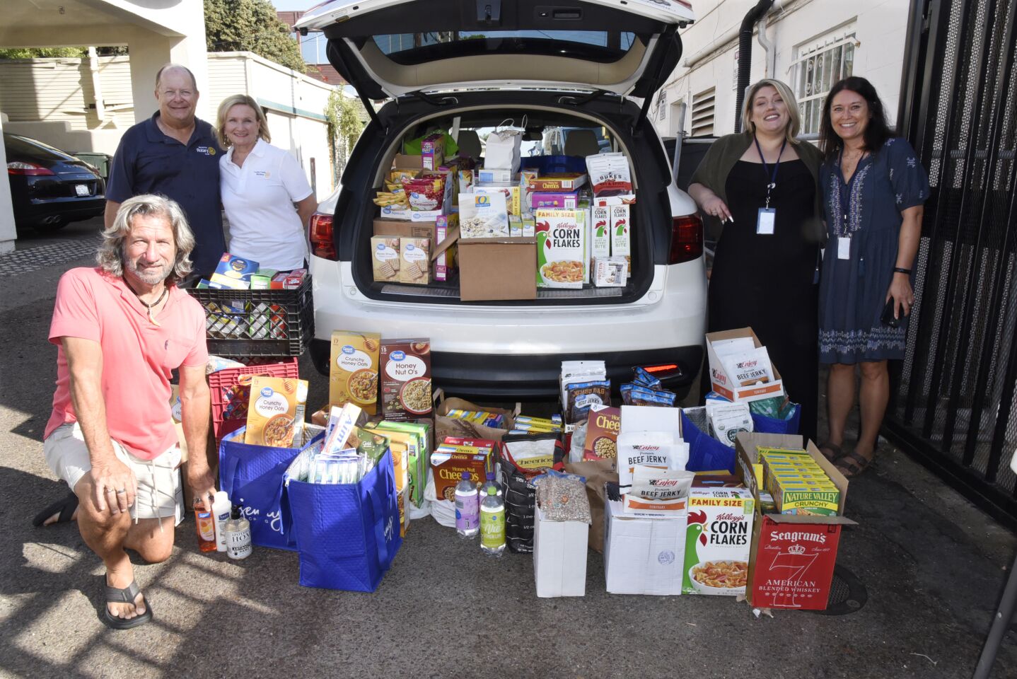 Encinitas Rotary President John Simonelli (kneeling), Encinitas Rotary Community Services Director Mark Berning, Encinitas Coastal Rotary President Vembra Holnagel, CRC Director of Social Services Miranda Chavez, Volunteer Manager Sara Rosenbaum, with the food donations the two Encinitas Rotary groups collected