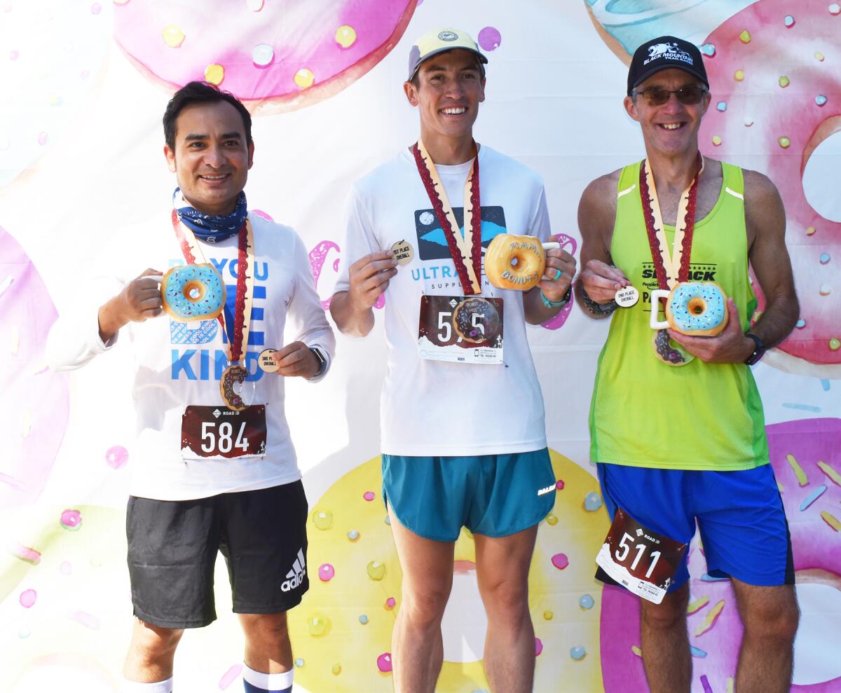 Donut Mile male finishers Diwakar Thapa, JJ Goodrich and Greg Bergeron holding their medals and prize, a doughnut-shaped mug.